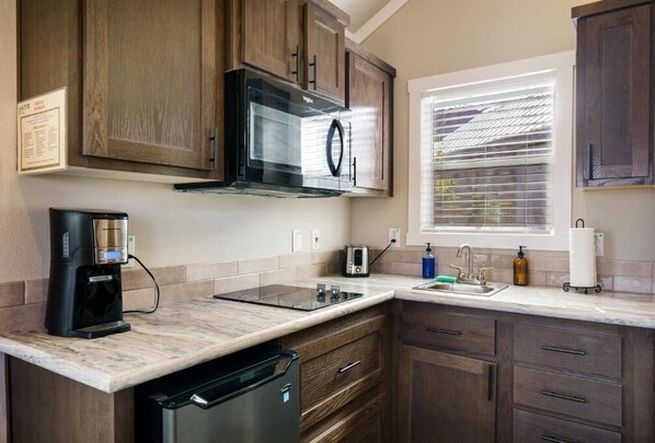 A modern kitchen with wooden cabinets, a built-in microwave, a coffee maker, and a window with blinds. - HTR Moab (Moab)
