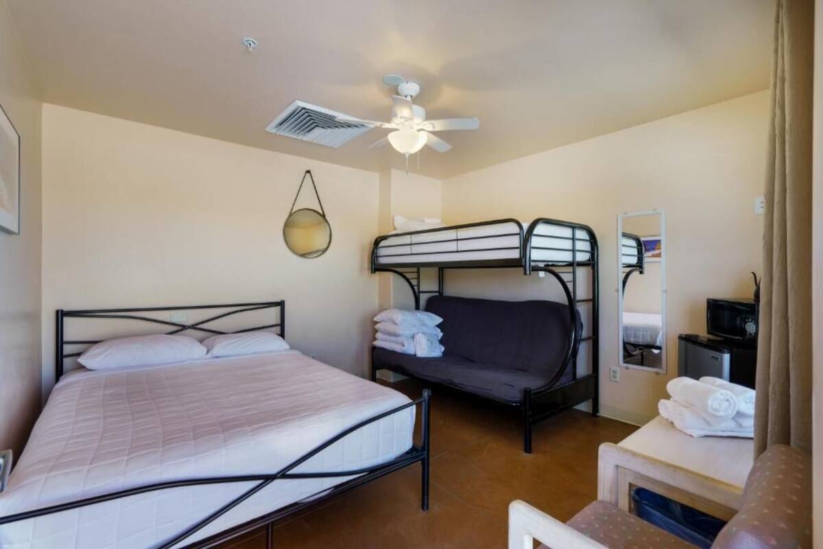 A bedroom with a single bed, a bunk bed, a ceiling fan, a small table with a mirror, and a television.