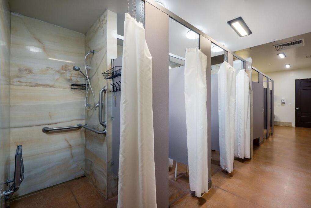 A row of white shower stalls with a marble wall and a handrail on the left.