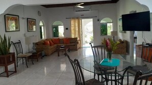 A spacious living area with a sofa, chairs, a dining table, and a TV. - Coco Gardens (Negril)