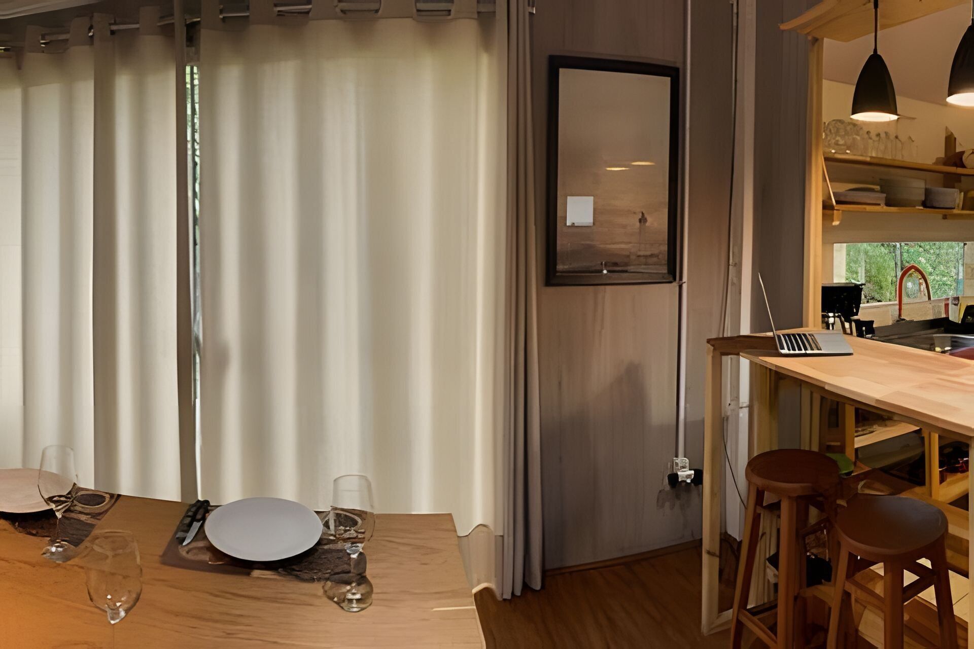 A dining area with a wooden table set for two, a laptop on the table, and a bar stool.