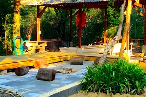A covered outdoor area with a stone floor, wooden benches, and a pergola structure. - Villa dos Sonhos Vá de Caiaque Até o Mar (São Francisco do Sul)