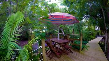 A wooden deck with a table and chairs, an umbrella, and lush greenery.