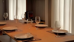A dining area with a long table set for four, a hanging light fixture, and a television in the background. - Villa dos Sonhos Vá de Caiaque Até o Mar (São Francisco do Sul)