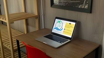 Una computadora portátil sobre una mesa de madera con una silla roja, un cuadro en la pared y una estructura de literas.