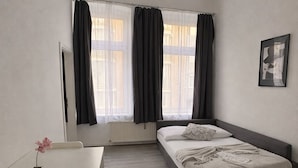 Une chambre à coucher moderne avec un lit, une petite table sur laquelle est posé un vase, et une fenêtre avec des rideaux.