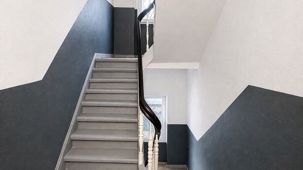 Un escalier moderne avec des marches en bois et des murs sombres, menant à un palier doté d’une fenêtre.