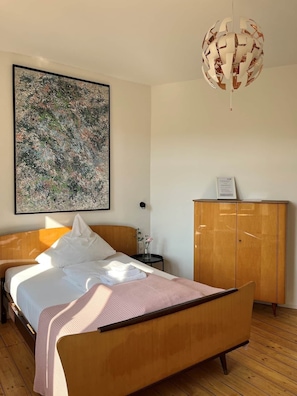 Ein Schlafzimmer mit einem hölzernen Bett, einem großen abstrakten Gemälde, einem Holzschrank und einer Pendelleuchte.