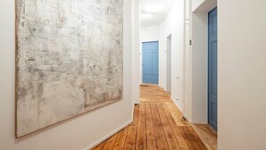 A hallway with wooden flooring, white walls, and a large abstract painting on the left. - Artist's room 1.5 - the minimalist (Gera)