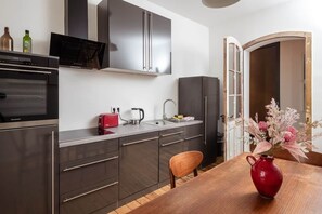 A modern kitchen with stainless steel appliances, a wooden dining table, and a vase with flowers. - Artist's room 1.5 - the minimalist (Gera)