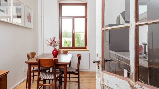 A dining area with a wooden table and chairs, a window with a view, and a door with a rustic design. - Artist's room 1.5 - the minimalist (Gera)