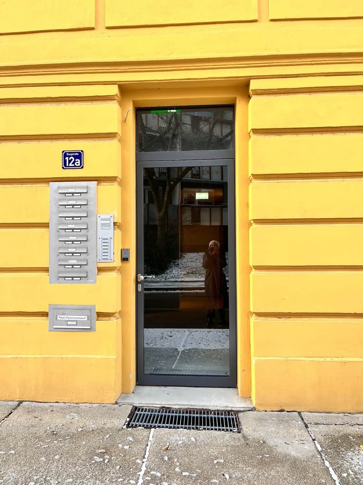 Un edificio amarillo con una puerta, un buzón y un letrero que indica '12a'.