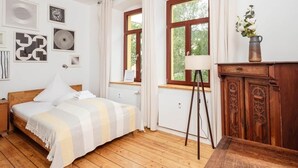 Une chambre à coucher avec un lit en bois, des rideaux blancs, une lampe sur pied et une armoire en bois.