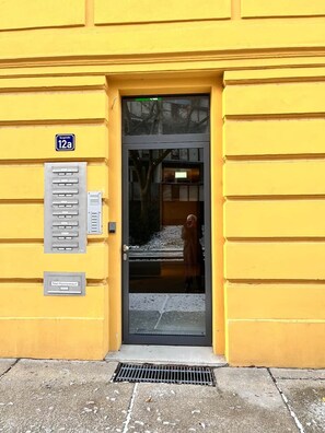 Un bâtiment jaune avec une porte, une boîte aux lettres et une enseigne indiquant « 12a ».