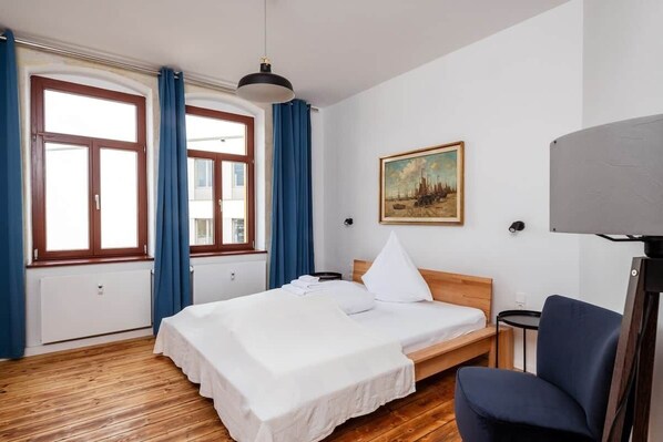 Ein Hotelzimmer mit Holzboden, einem Bett mit weißer Bettwäsche, einem Gemälde an der Wand und einem Schreibtisch mit Lampe.