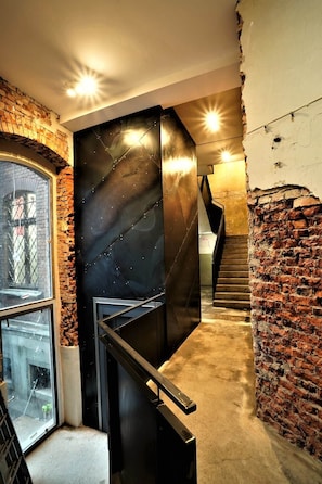 Un escalier moderne avec une rampe en métal noir, des murs en briques et une fenêtre en verre sur le côté gauche.