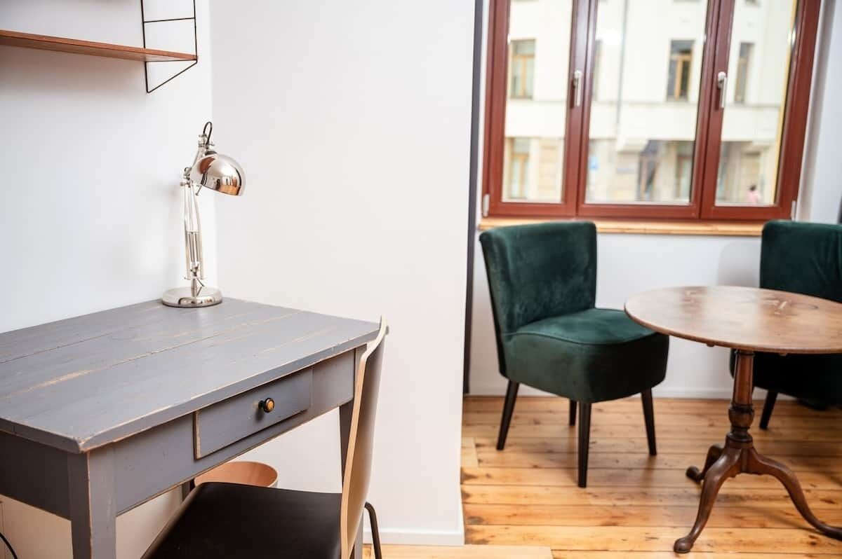 A room with a desk, a chair, a round table, and a window with a view of buildings.