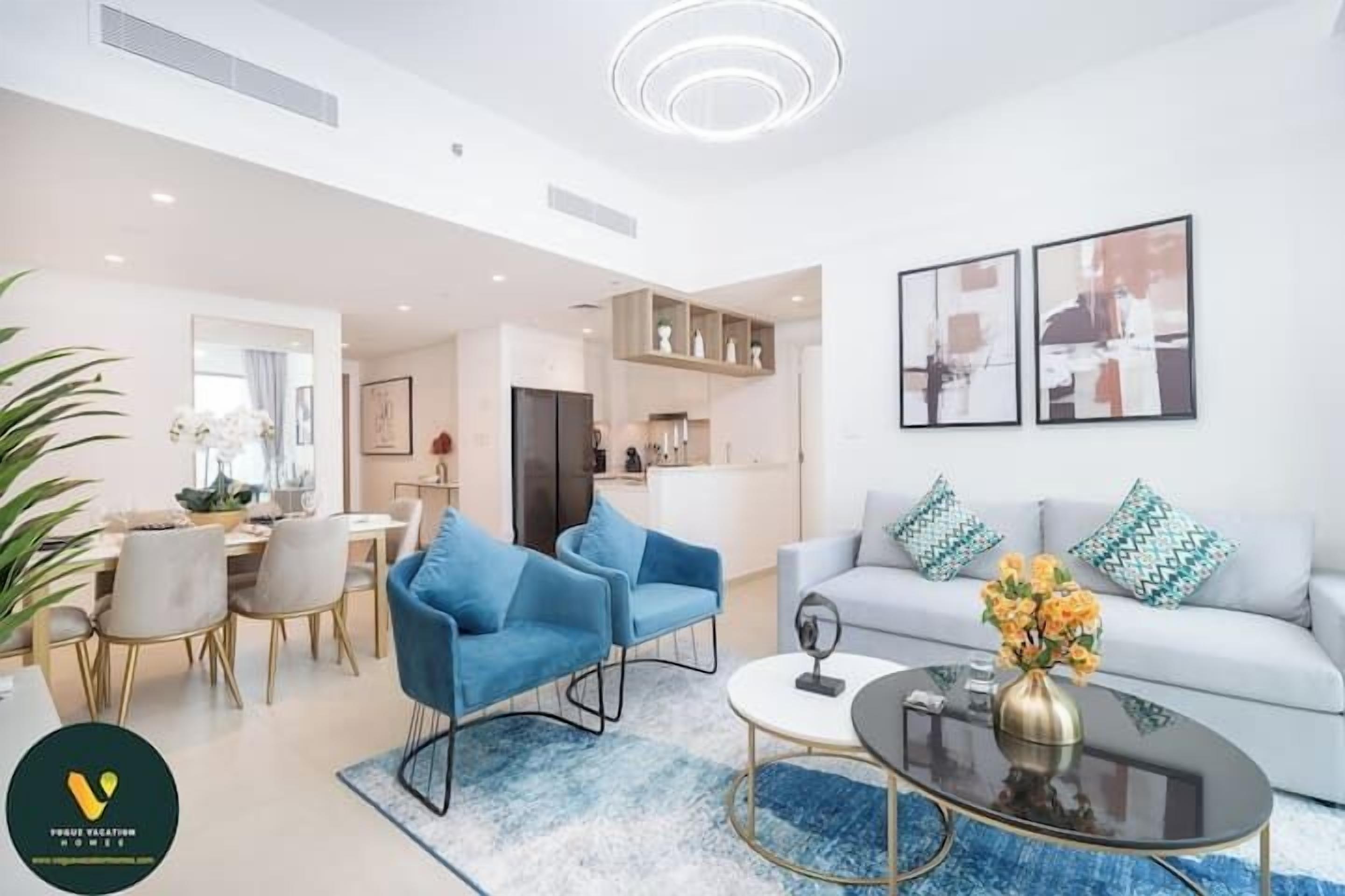 Uma sala de estar moderna com um sofá, duas poltronas azuis, uma mesa de centro e um espaço de jantar com uma mesa e cadeiras.