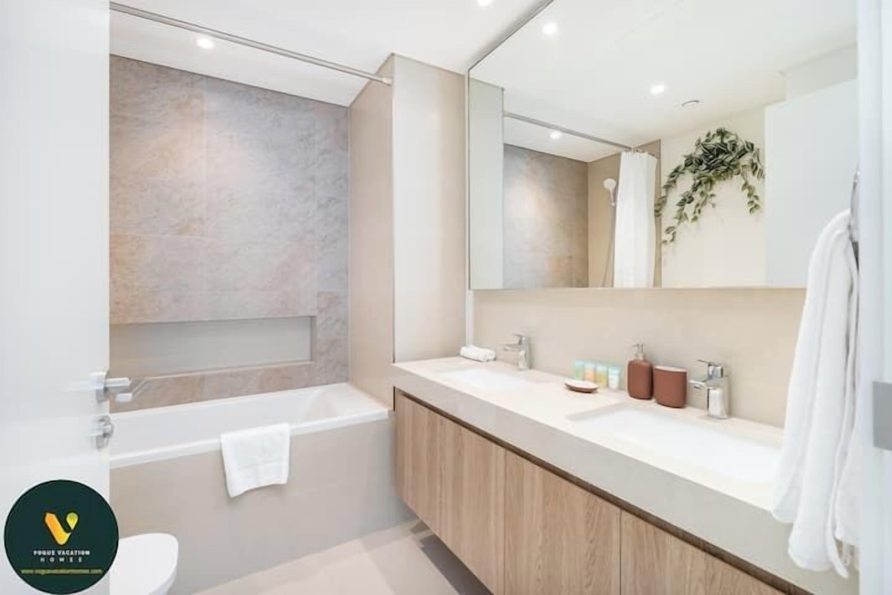 A modern bathroom with a bathtub, a large mirror, and a vanity with a sink and toiletries.