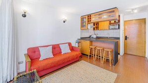 Un espacio habitable compacto con kitchenette, un sofá con cojines y una pequeña zona de bar con taburetes.