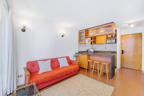 A compact living space with a kitchenette, a sofa with cushions, and a small bar area with stools. - Portugal Chic - 1D Piscina & Gimnasio (Santiago)