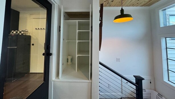 Eine Treppe mit Holzboden, einer hängenden Pendelleuchte und Blick auf einen Schrank mit Regalen.