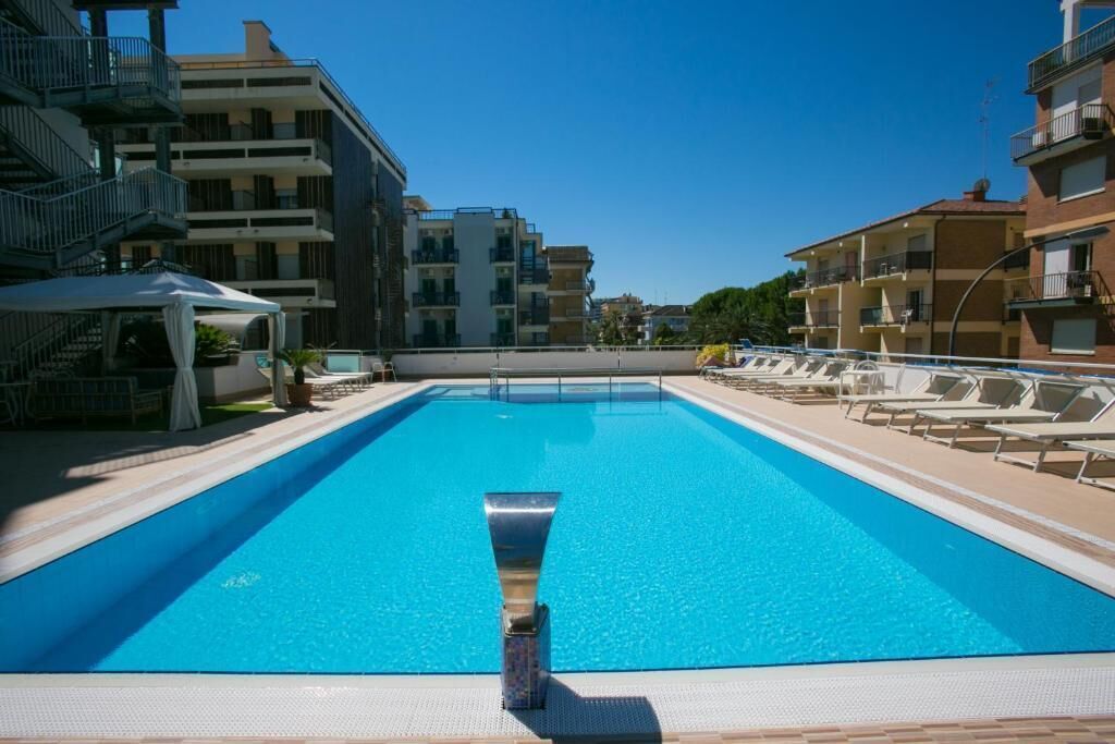 Une piscine rectangulaire dotée d’un élément décoratif central, entourée de chaises longues et d’un espace salon abrité.