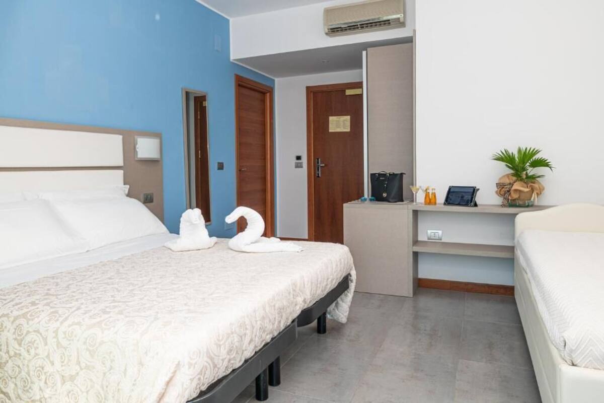 Une chambre d’hôtel avec un lit, un bureau et une chaise. On y trouve une porte et un climatiseur fixé au mur.