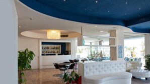 Een moderne hotellobby met een gebogen plafond, een zithoek met een witte bank en een bar met een drankendisplay.