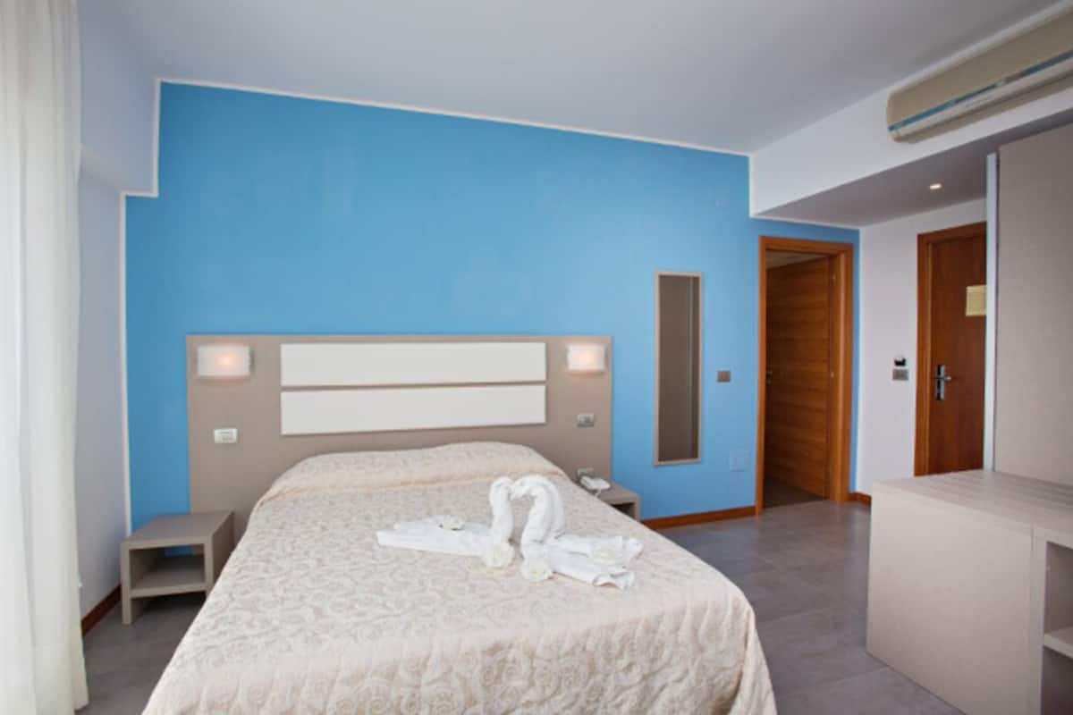 Une chambre d’hôtel avec un grand lit, une table de chevet, une commode, un miroir et une armoire.