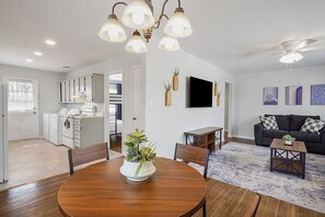 A modern living room with a dark grey sofa, a wooden coffee table, and a dining area with a wooden table and chairs. There is a TV mounted on the wall and a ceiling fan. - Vestavia 3 BR Convenient Location (Vestavia Hills)