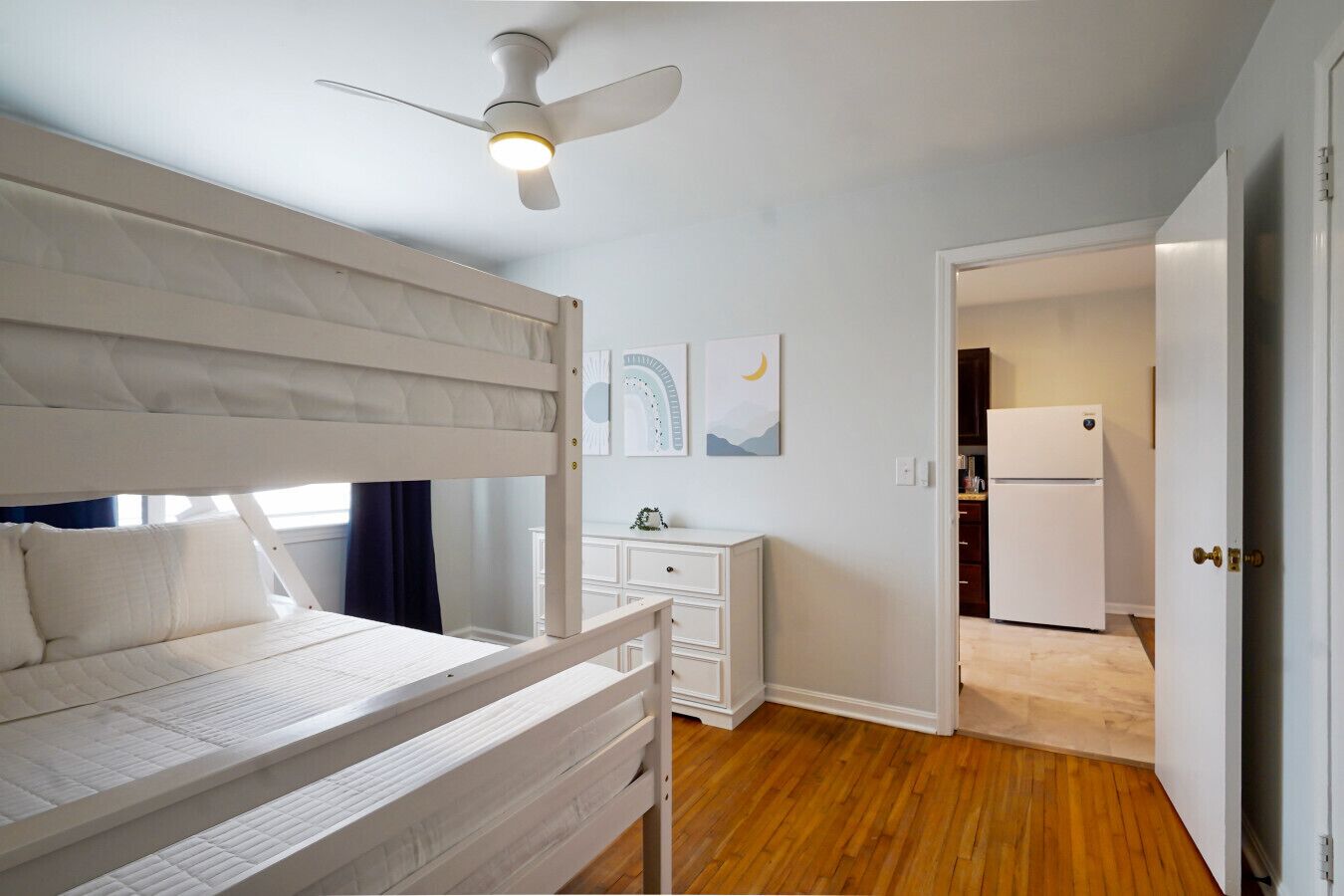 Een slaapkamer met een stapelbed, een plafondventilator, een dressoir en uitzicht op de keuken.