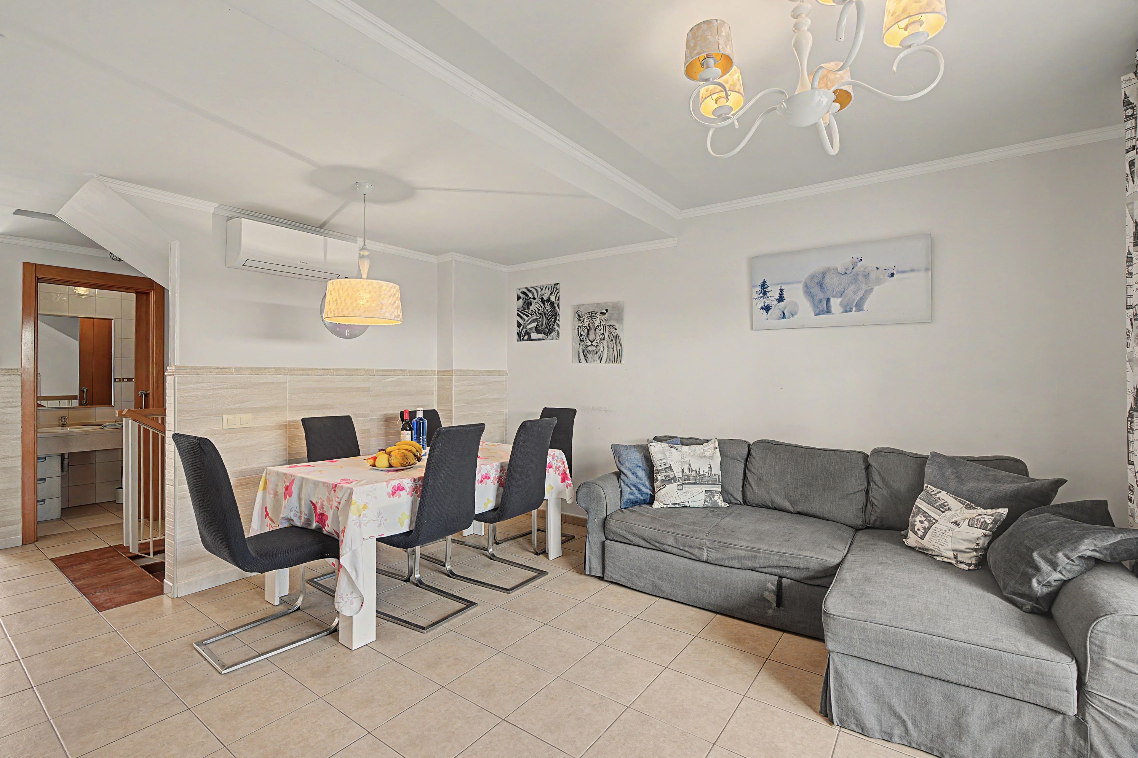 A modern living room with a grey sofa, a dining table with chairs, and a kitchen area with a wooden door.
