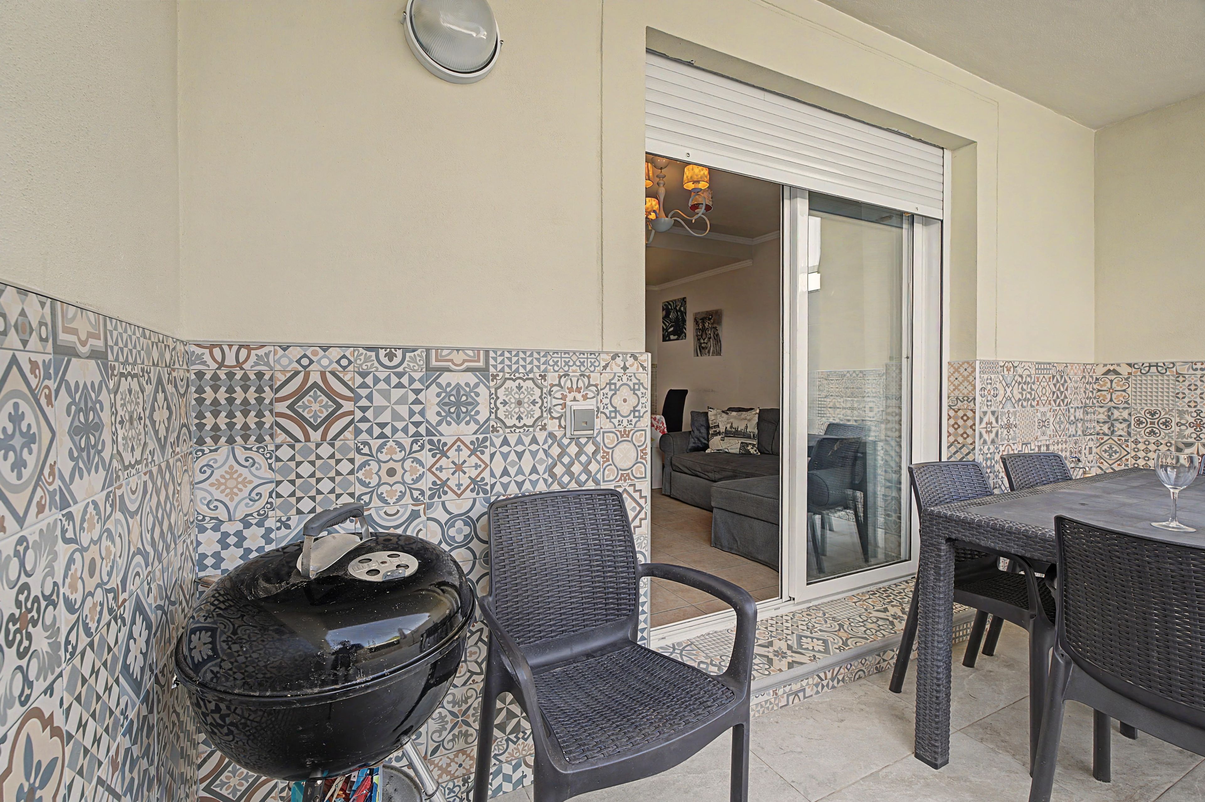 A patio area with a grill, outdoor furniture, and patterned tiles.