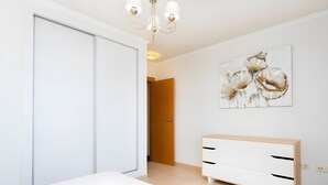 Ein Zimmer mit einem Bett, einem weißen Schminktisch, einer Kandelaber und einer Wand mit einem Blumenbild.