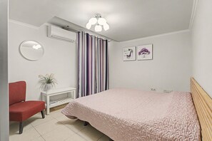 A bedroom with a bed, a chair, a bedside table, a mirror, a window with curtains, and wall art. - Vacation Apartment 'Oasis Fañabe Townhouse' with Mountain View, Wi-Fi and Air Conditioning (Costa Adeje)