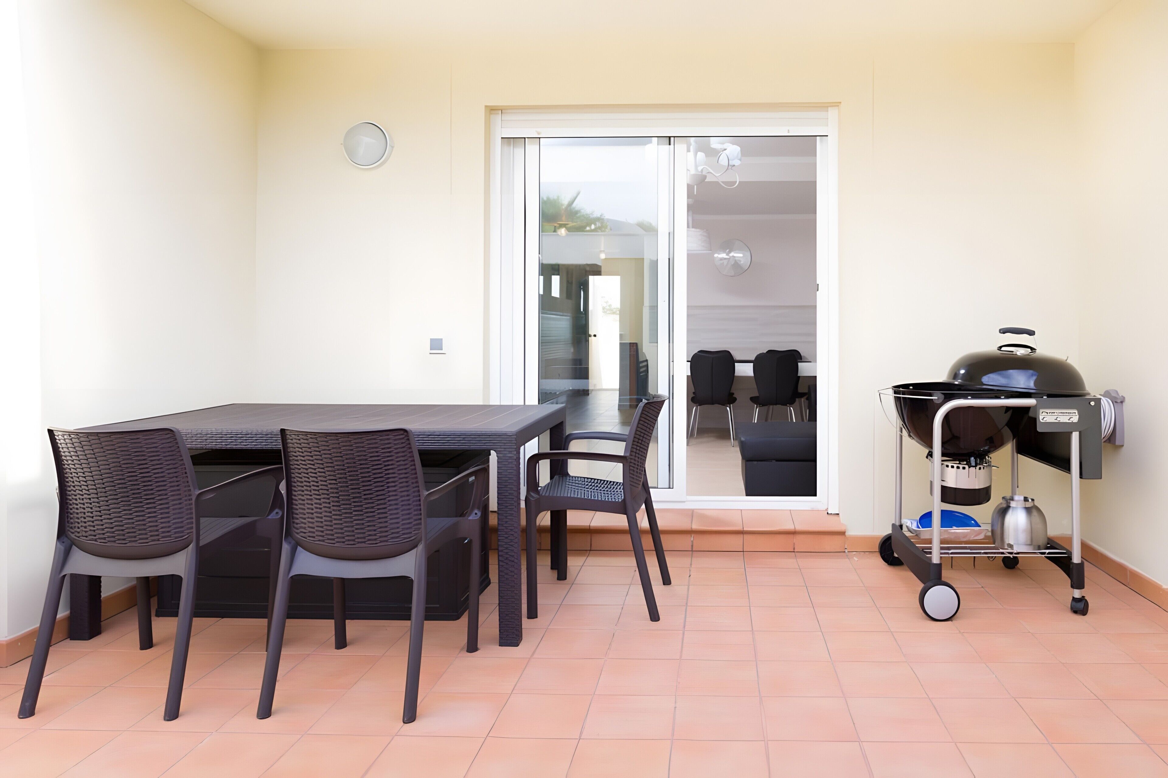 Une terrasse avec une table et des chaises, une porte-fenêtre coulissante et un barbecue.