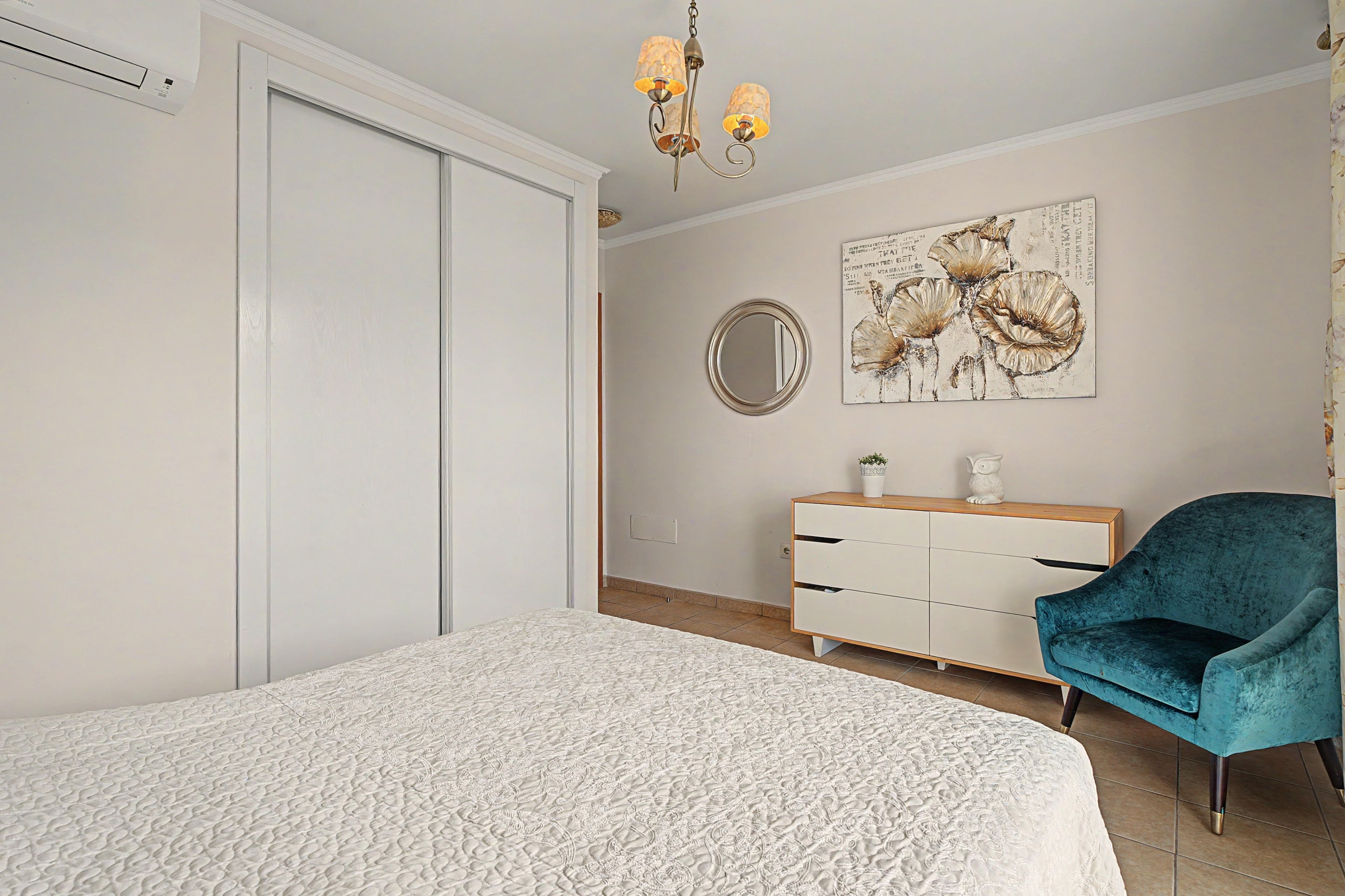 Un dormitorio con una cama, un aparador, una silla, un espejo y una obra de arte colgada en la pared.