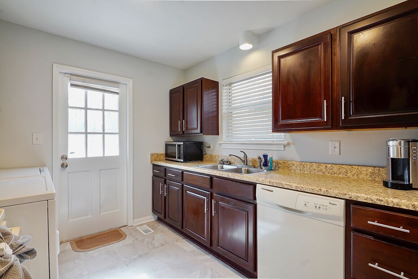 A kitchen with dark wooden cabinets, a granite countertop, a microwave, a coffee maker, and a dishwasher.