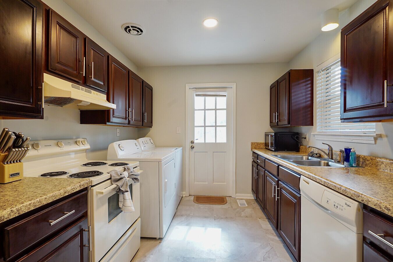 A kitchen with dark wooden cabinets, a white stove, a washing machine, and a dishwasher.