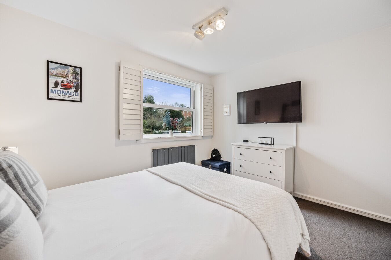 A bedroom with a bed, a dresser, a TV, and a window with shutters.