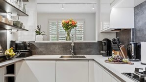 Een moderne keuken met een centraal eiland, een inbouwspoelbak en een raam met zonwering.