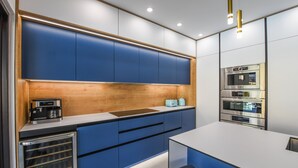 Eine moderne Küche mit blauen Schränken, einer Holzvertäfelung und eingebauten Geräten, darunter eine Kaffeemaschine und ein Backofen.