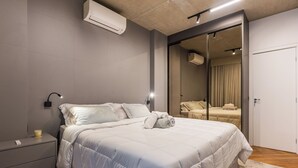 Une chambre moderne dotée d’un grand lit, de tables de chevet, d’un appareil de climatisation et d’une porte coulissante donnant accès à une salle de bain.