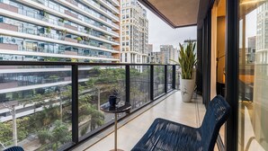 Un balcon donnant sur des immeubles de grande hauteur, un pot de fleurs et une table avec une chaise.