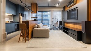 Une cuisine moderne dotée d’appareils électroménagers intégrés, un coin repas avec un bar, un espace salon avec un canapé et des fauteuils, et un grand téléviseur à écran plat fixé au mur.
