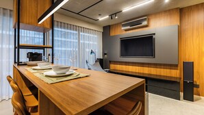 Une cuisine moderne avec une table à manger en bois, des appareils électroménagers intégrés et un grand téléviseur à écran plat fixé au mur.