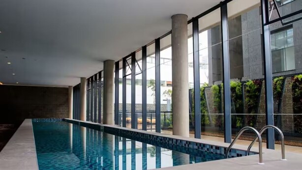 Une piscine intérieure avec des parois en verre transparent, de grandes fenêtres et un design moderne.