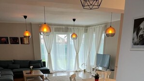 En moderne stue med sofa, sofabord og spiseplads med stole samt et fjernsyn.