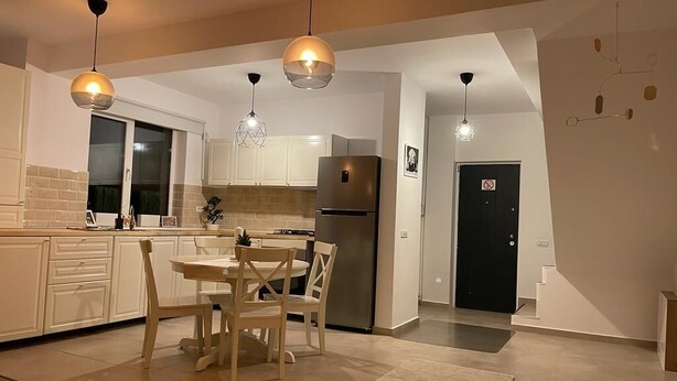Et moderne køkken med hvide skabe, et rustfrit stål køleskab og et spiseområde med træstole.